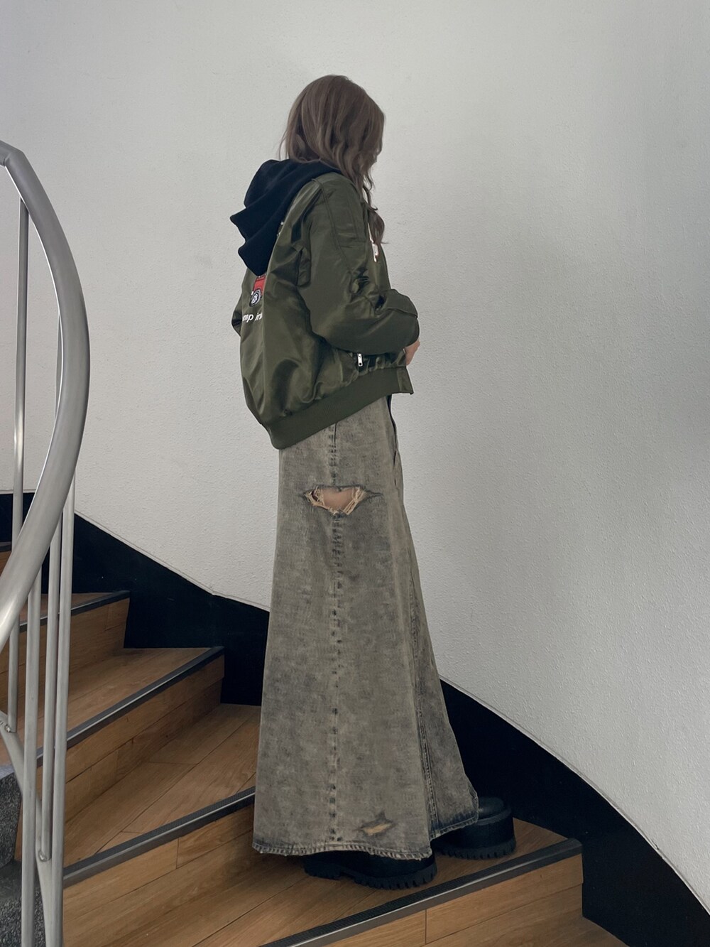 グリーン系のブルゾン、ブルー系のデニムスカート、ブラック系のブーツを着用したレディースの秋コーディネートの4枚目の写真