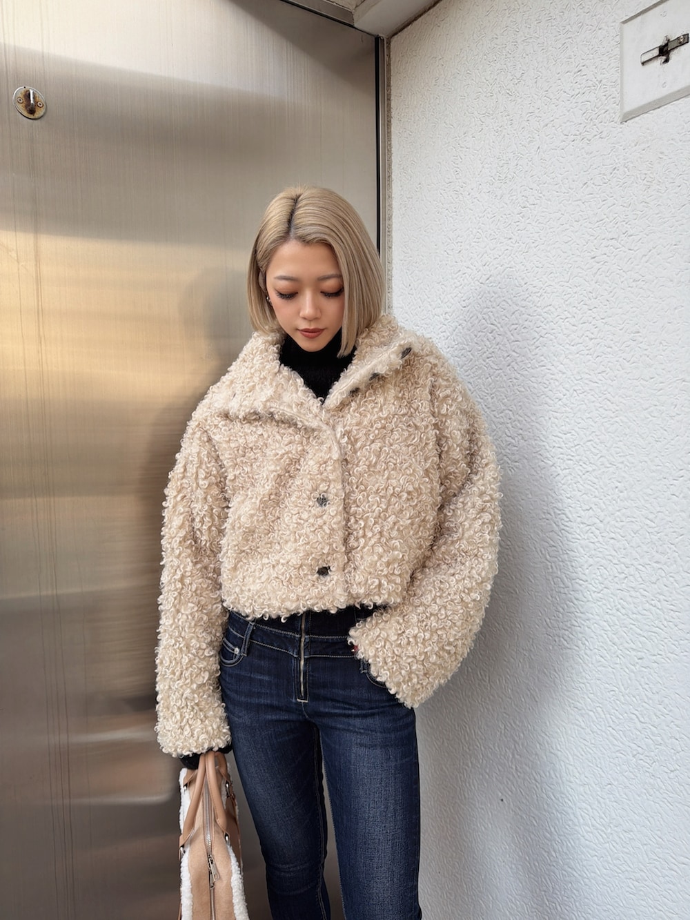 ホワイト系のブルゾン、ブルー系のデニムパンツ、ベージュ系のショルダーバッグを着用したレディースの冬コーディネートの3枚目の写真