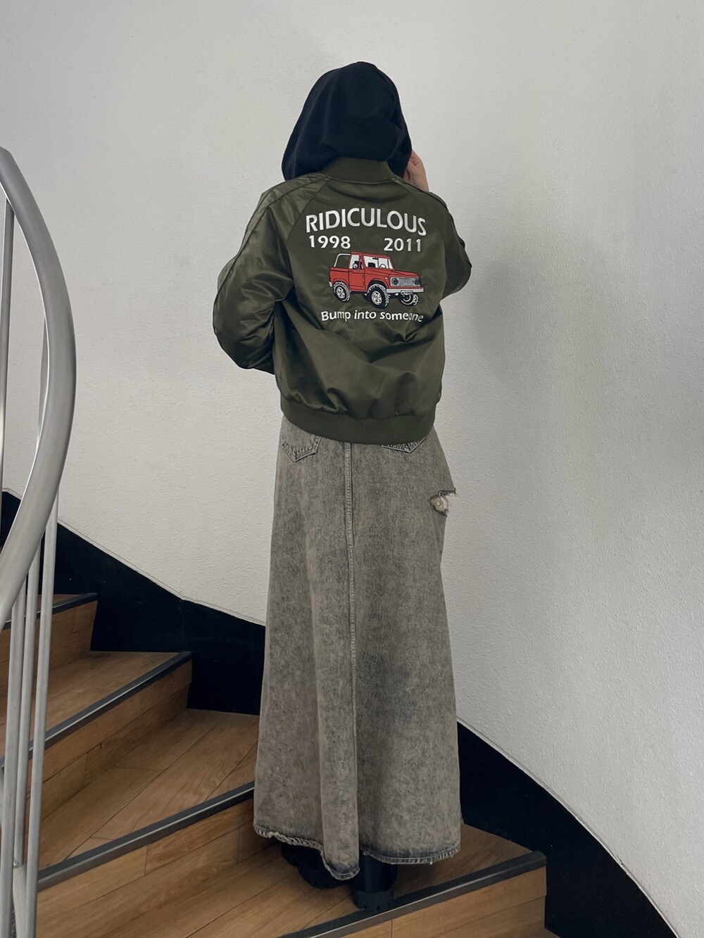 グリーン系のブルゾン、ブルー系のデニムスカート、ブラック系のブーツを着用したレディースの秋コーディネートの3枚目の写真