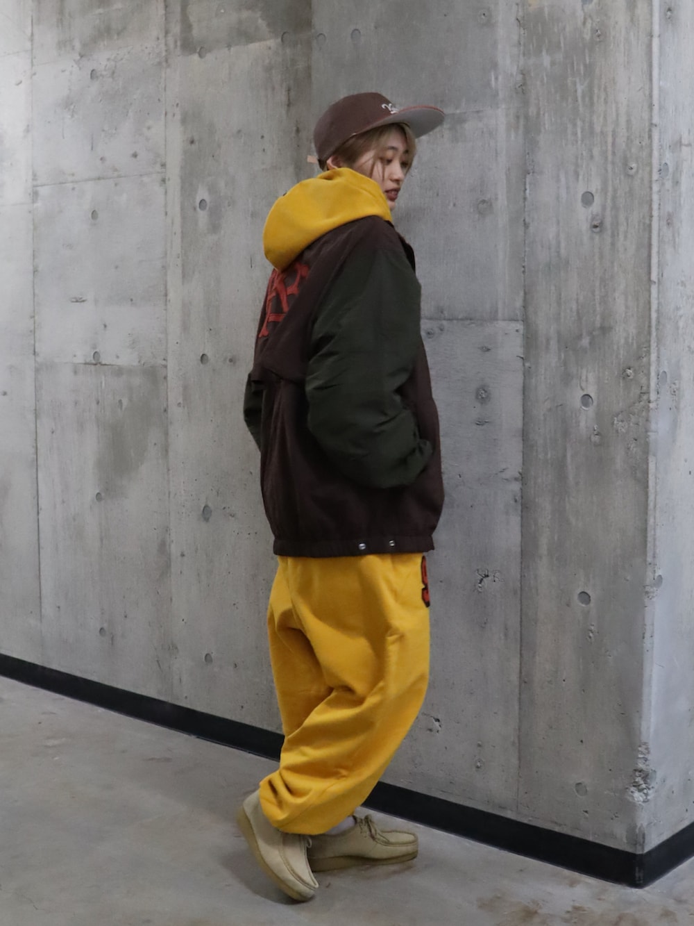 イエロー系のパーカー、イエロー系のスウェットパンツ、ブラウン系のナイロンジャケットを着用したレディースの春コーディネートの2枚目の写真