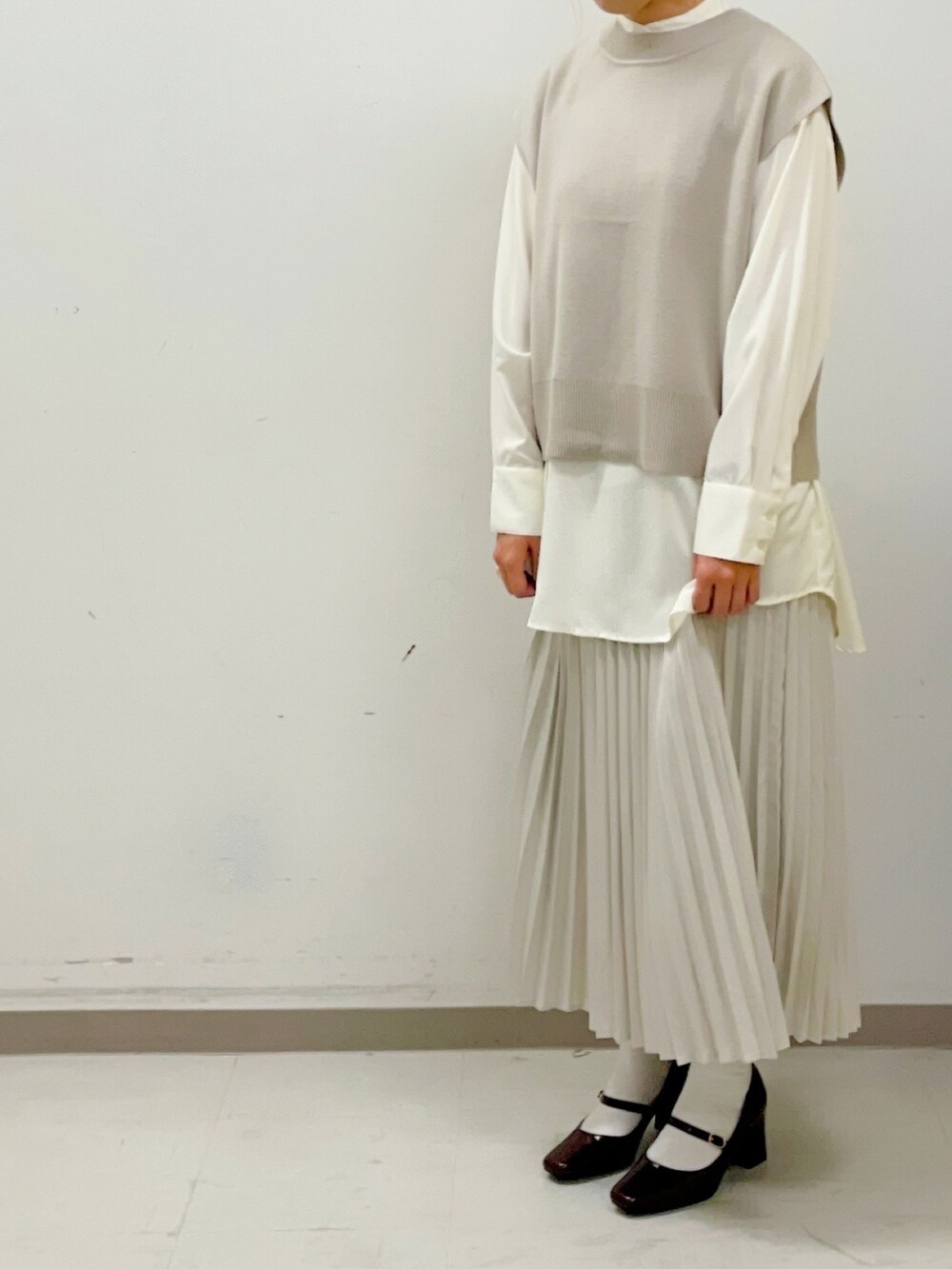 レッド系のパンプス、ホワイト系のスカート、ベージュ系のベストを着用したレディースの夏コーディネートの2枚目の写真