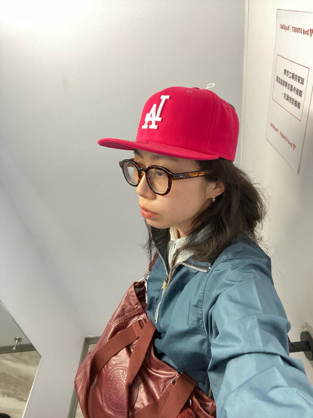 ブルー系のナイロンジャケット、レッド系のバッグ、ピンク系の帽子を着用したレディースの春コーディネートの2枚目の写真