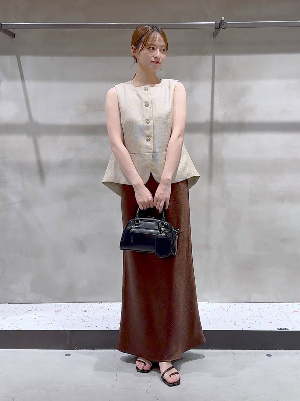 ブラウン系のスカート、ベージュ系のブルゾン、ブラック系のサンダルを着用したレディースの夏コーディネートの2枚目の写真