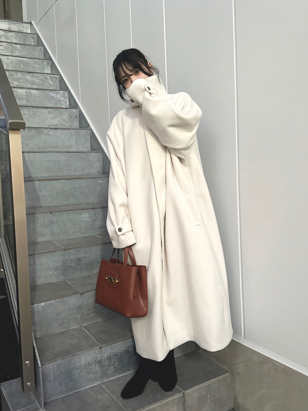 レッド系のバッグ、ホワイト系のステンカラーコート、ブラック系のブーツを着用したレディースの冬コーディネートの2枚目の写真