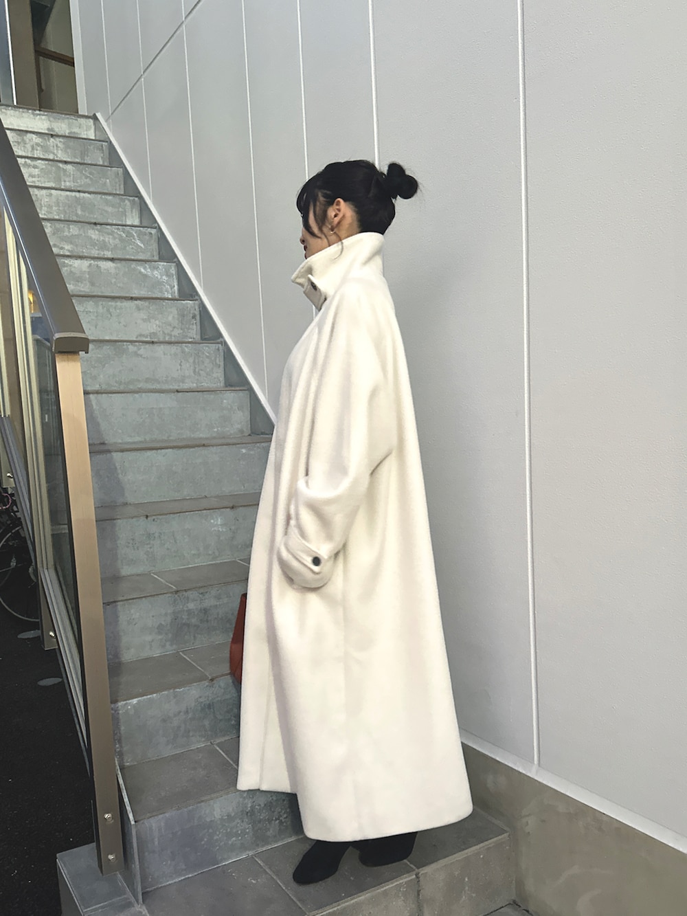 レッド系のバッグ、ホワイト系のステンカラーコート、ブラック系のブーツを着用したレディースの冬コーディネートの3枚目の写真