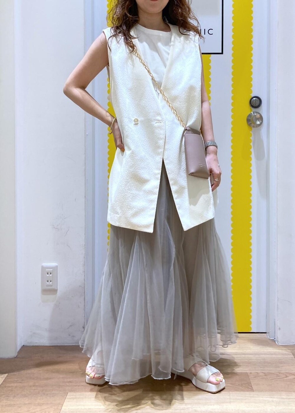 ホワイト系のサンダル、ベージュ系のショルダーバッグ、ホワイト系のベストを着用したレディースの春コーディネートの2枚目の写真