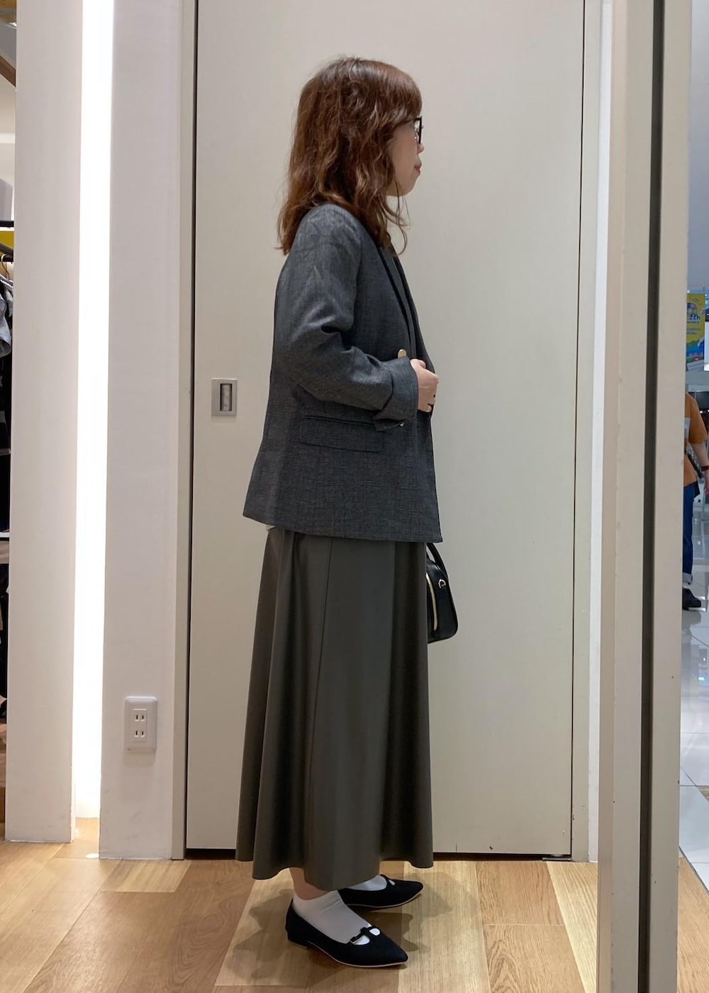 グレー系のテーラードジャケット、グリーン系のスカート、ブラック系のパンプスを着用したレディースの秋コーディネートの3枚目の写真