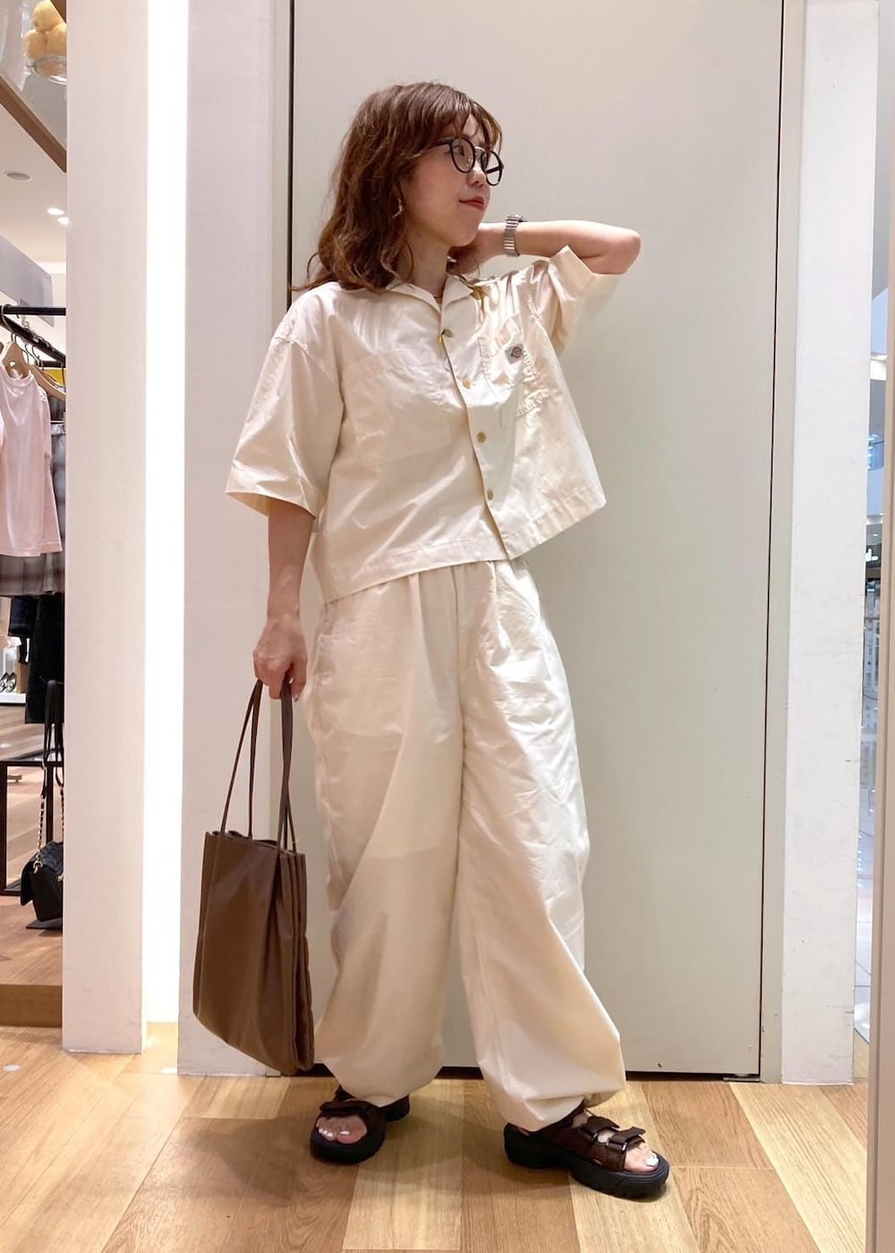 ブラウン系のトートバッグ、ブラウン系のサンダル、ホワイト系のシャツ/ブラウスを着用したレディースの夏コーディネートの2枚目の写真