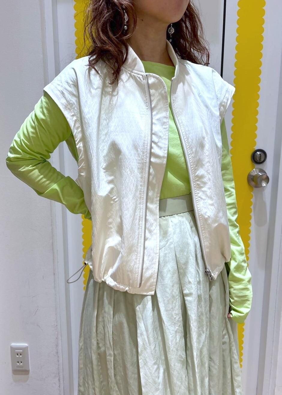 グリーン系のスカート、シルバー系のパンプス、ホワイト系のベストを着用したレディースの春コーディネートの2枚目の写真