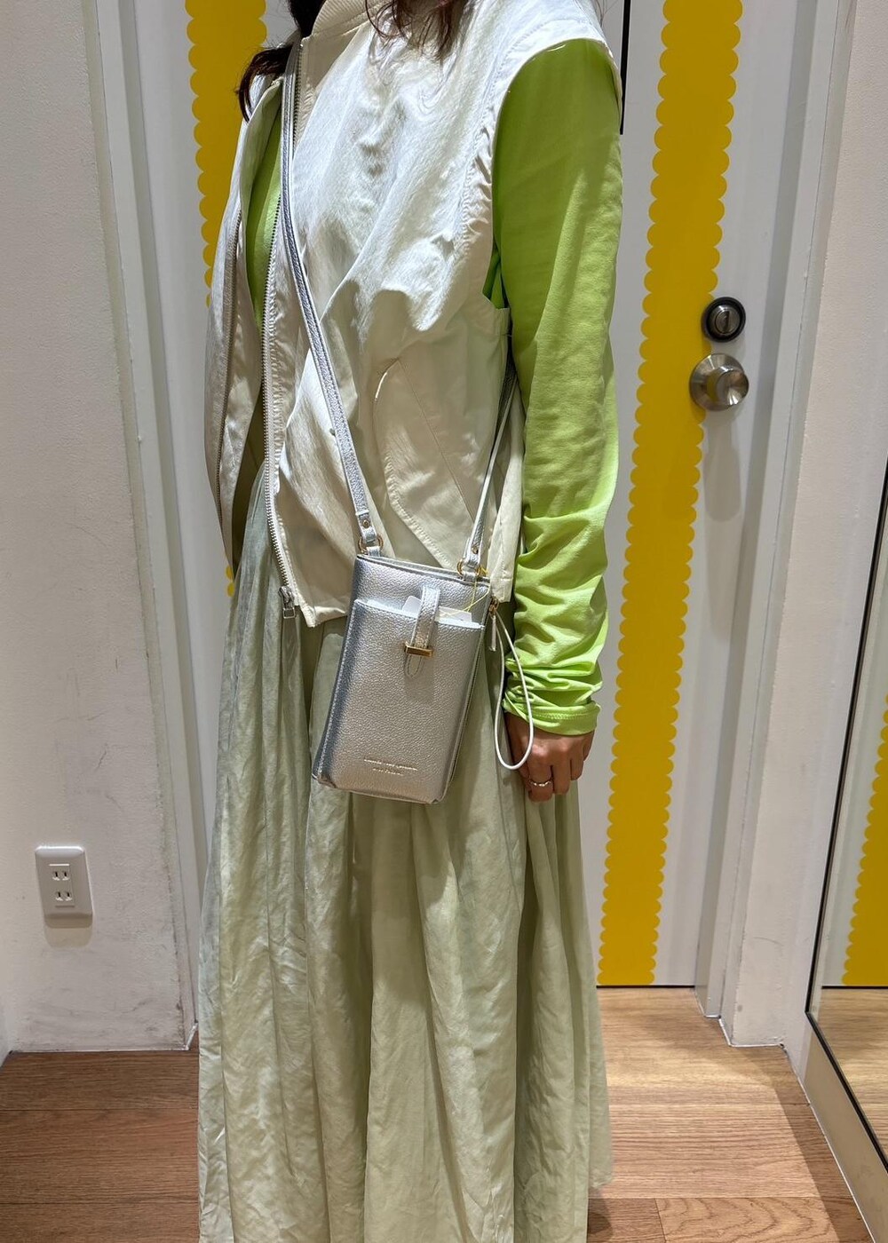 グリーン系のスカート、シルバー系のパンプス、ホワイト系のベストを着用したレディースの春コーディネートの4枚目の写真