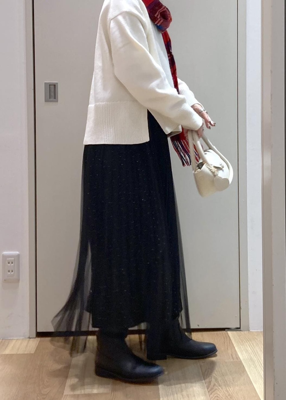 ブラック系のスカート、ホワイト系のニット/セーター、ブラック系のブーツを着用したレディースの冬コーディネートの2枚目の写真