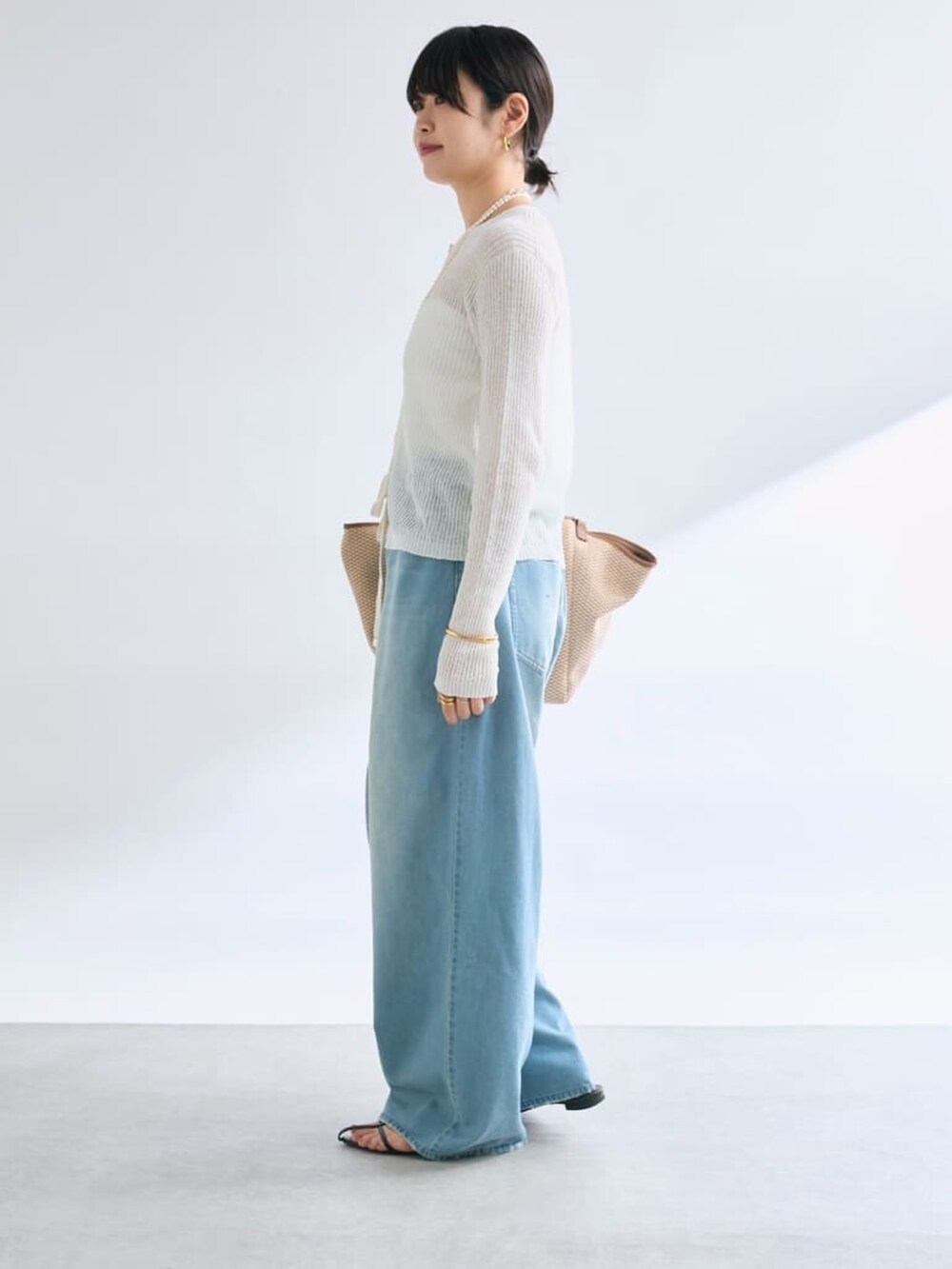 ブルー系のデニムパンツ、ホワイト系のカーディガン/ボレロ、ブラウン系のトートバッグを着用したレディースの夏コーディネートの2枚目の写真
