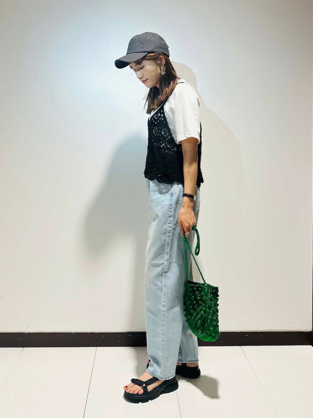 グリーン系のショルダーバッグ、ブルー系のデニムパンツ、ブラック系のキャップを着用したレディースの夏コーディネートの3枚目の写真
