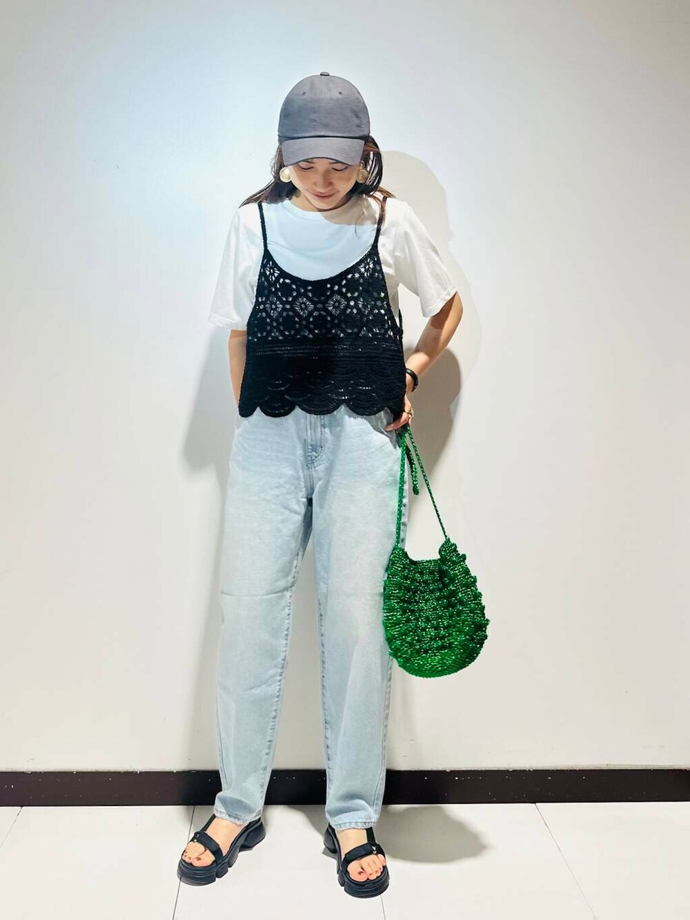 グリーン系のショルダーバッグ、ブルー系のデニムパンツ、ブラック系のキャップを着用したレディースの夏コーディネートの2枚目の写真