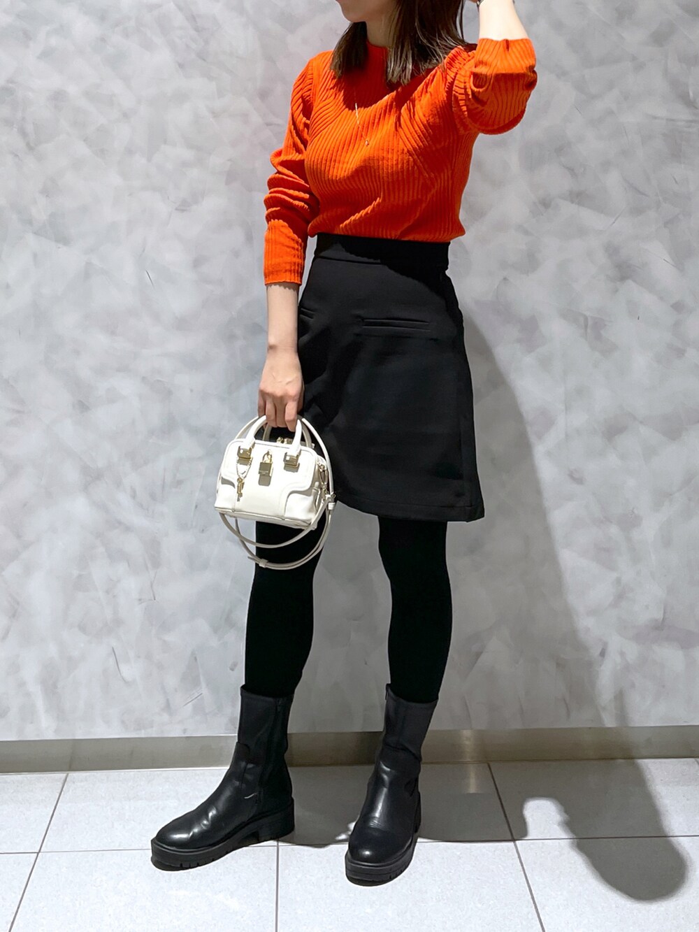 ホワイト系のショルダーバッグ、ブラック系のブーツ、オレンジ系のニット/セーターを着用したレディースの冬コーディネートの2枚目の写真