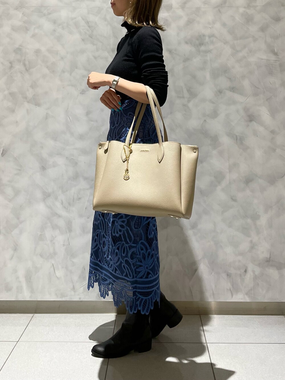 ベージュ系のトートバッグ、ブルー系のスカート、ブラック系のニット/セーターを着用したレディースの冬コーディネートの3枚目の写真