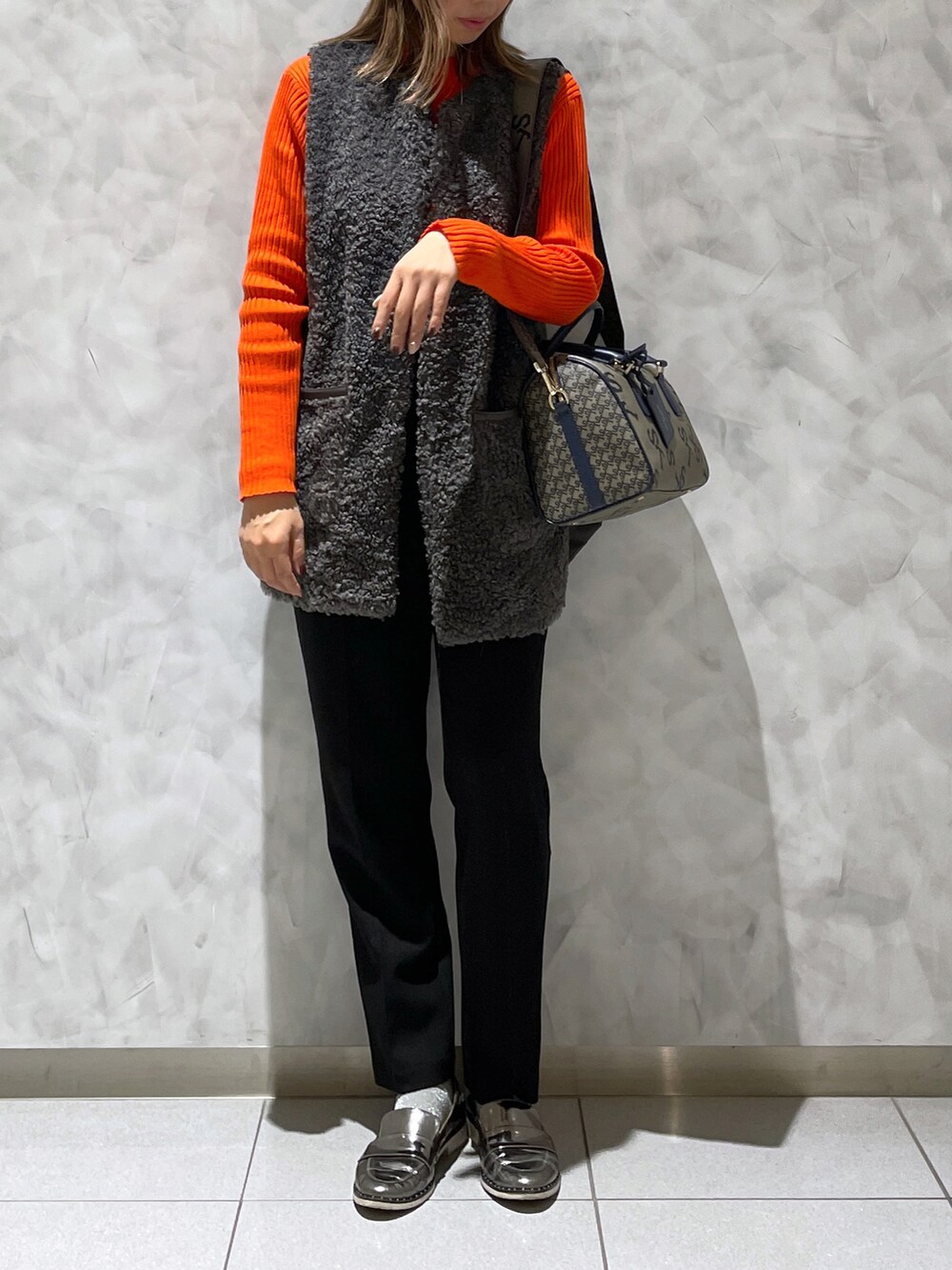 ブラウン系のボストンバッグ、グレー系のベスト、オレンジ系のニット/セーターを着用したレディースの冬コーディネートの3枚目の写真