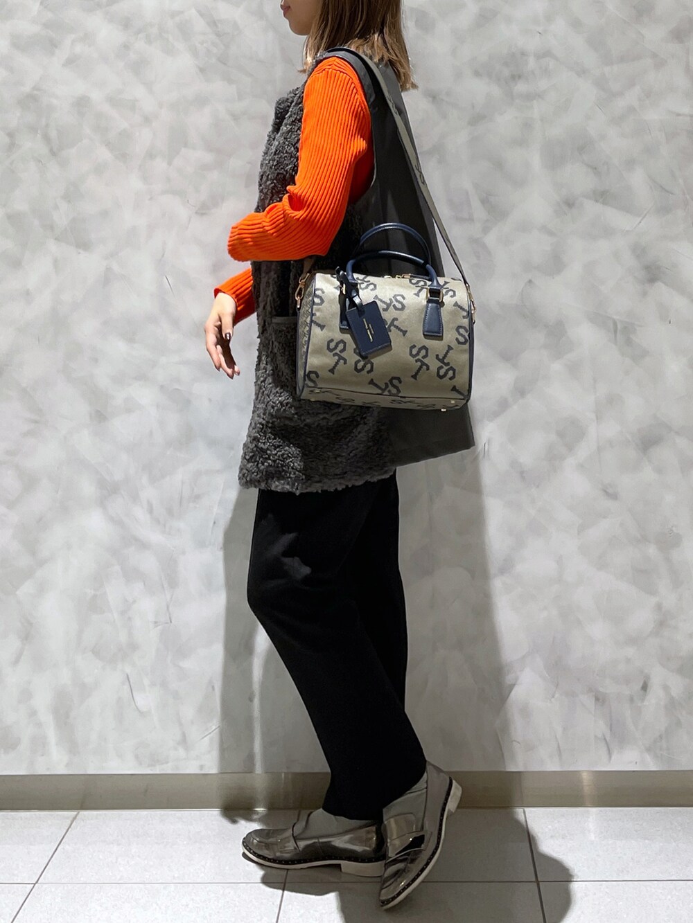 ブラウン系のボストンバッグ、グレー系のベスト、オレンジ系のニット/セーターを着用したレディースの冬コーディネートの4枚目の写真