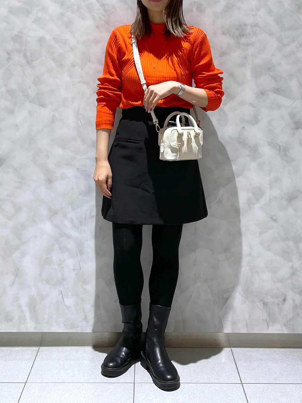 ホワイト系のショルダーバッグ、ブラック系のブーツ、オレンジ系のニット/セーターを着用したレディースの冬コーディネートの4枚目の写真