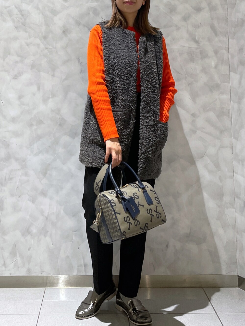 ブラウン系のボストンバッグ、グレー系のベスト、オレンジ系のニット/セーターを着用したレディースの冬コーディネートの2枚目の写真