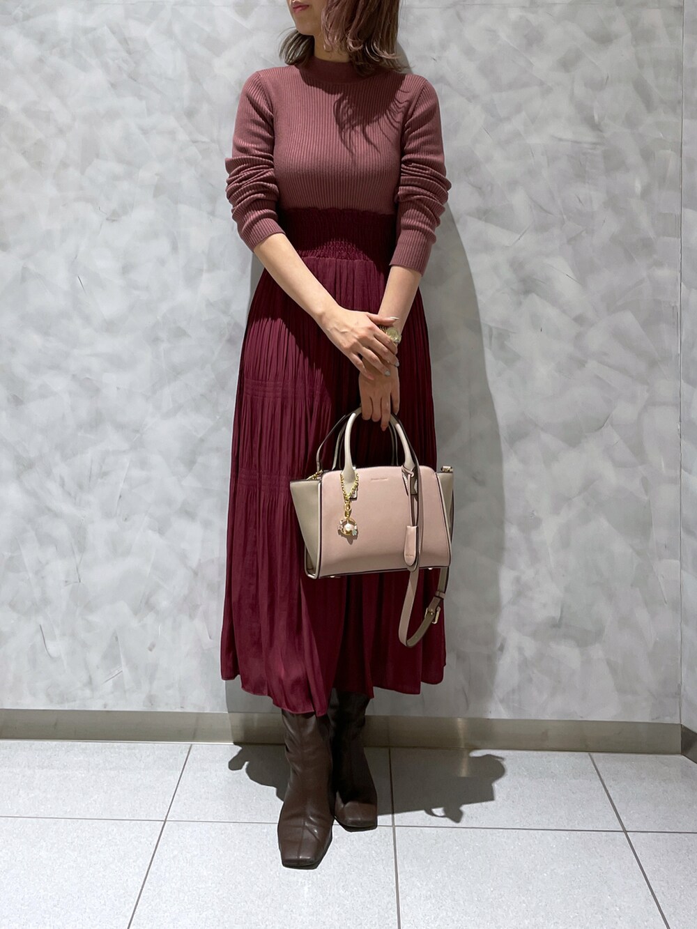 レッド系のワンピース、ブラウン系のブーツ、ピンク系のハンドバッグを着用したレディースの冬コーディネートの2枚目の写真