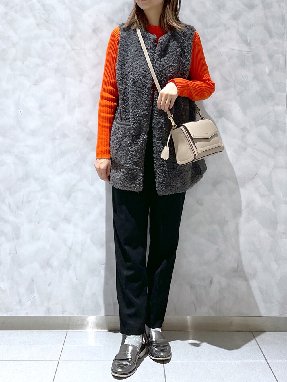 ブラック系のショルダーバッグ、グレー系のベスト、オレンジ系のニット/セーターを着用したレディースの冬コーディネートの2枚目の写真
