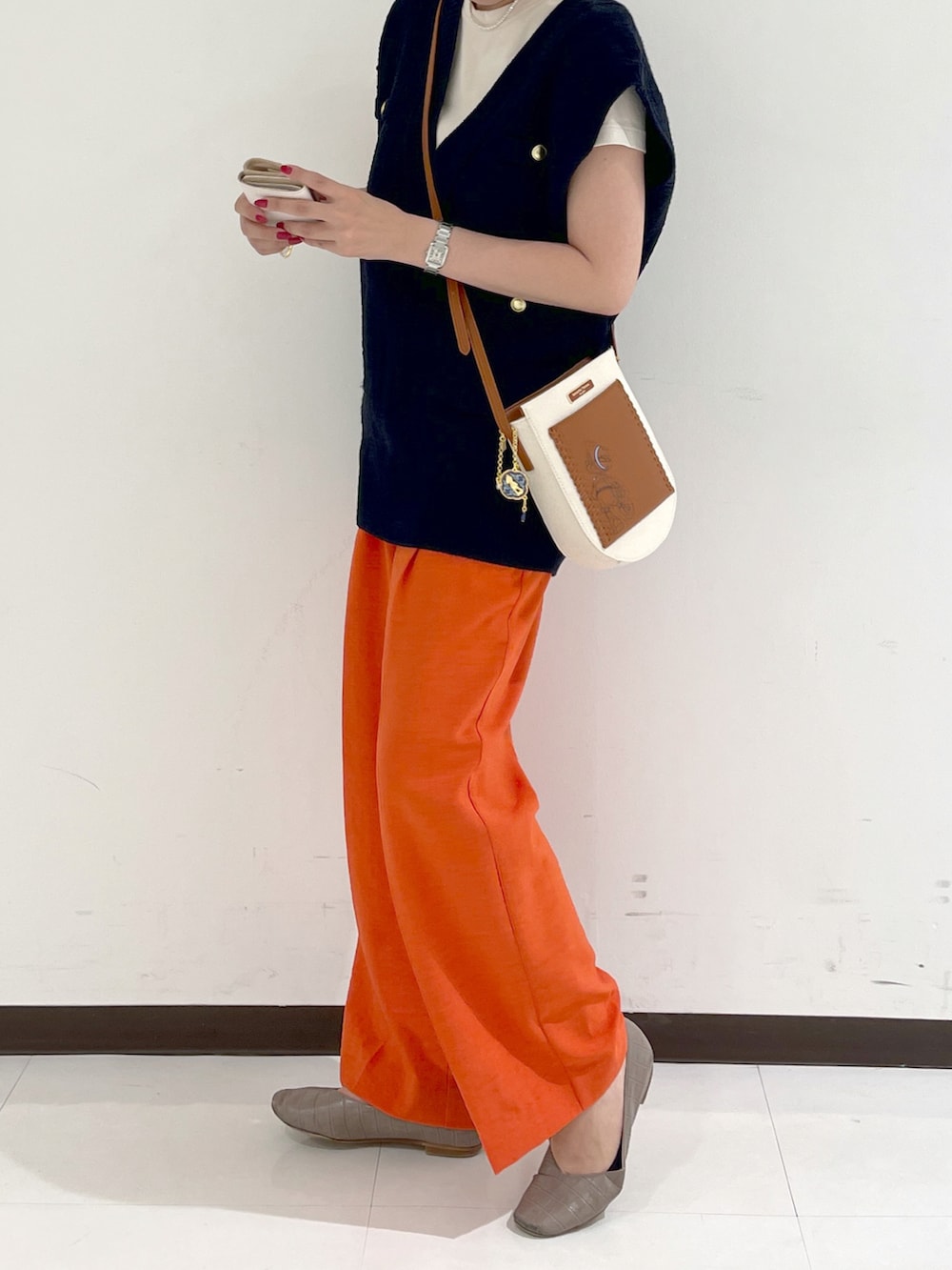 ブラウン系のショルダーバッグ、オレンジ系のスラックス、ブルー系のベストを着用したレディースの秋コーディネートの2枚目の写真