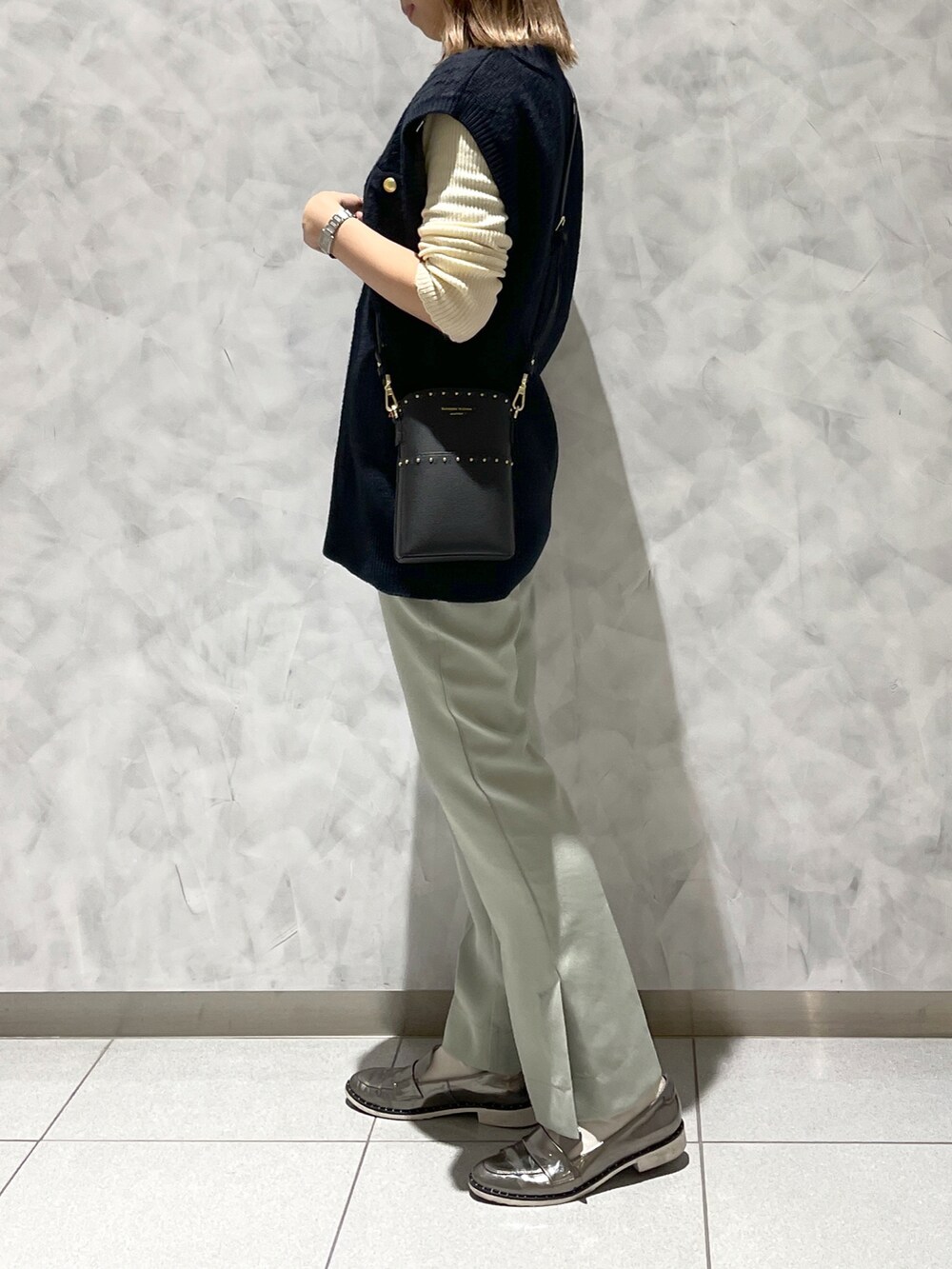 グレー系のシューズ、ブルー系のベスト、ブラック系のショルダーバッグを着用したレディースの冬コーディネートの3枚目の写真