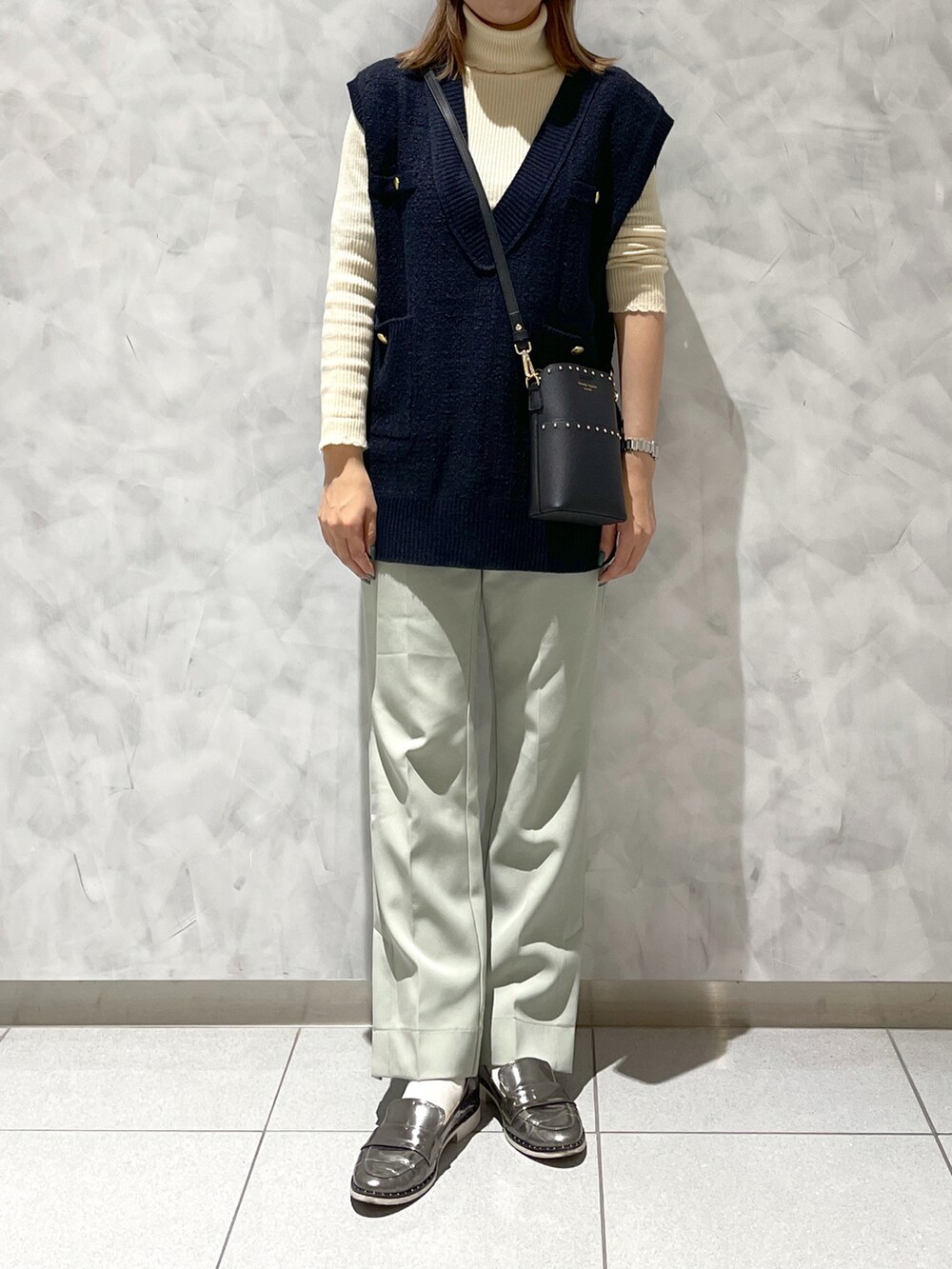 グレー系のシューズ、ブルー系のベスト、ブラック系のショルダーバッグを着用したレディースの冬コーディネートの4枚目の写真