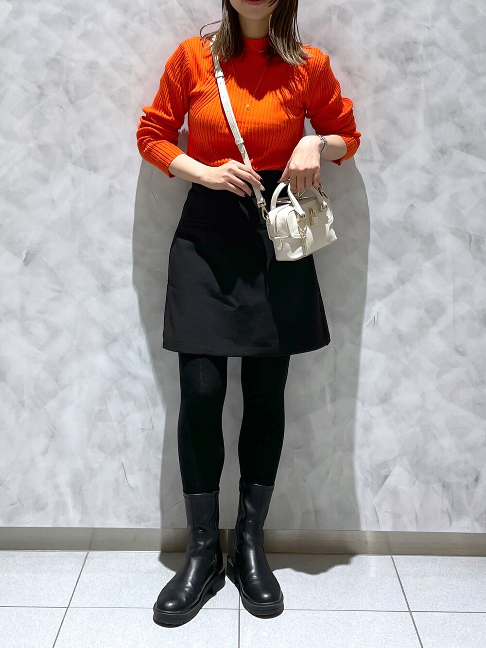 ホワイト系のショルダーバッグ、ブラック系のブーツ、オレンジ系のニット/セーターを着用したレディースの冬コーディネートの3枚目の写真
