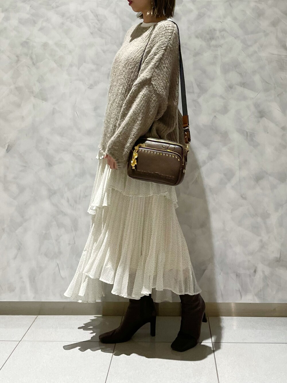 ブラウン系のブーツ、ホワイト系のスカート、ベージュ系のニット/セーターを着用したレディースの冬コーディネートの2枚目の写真