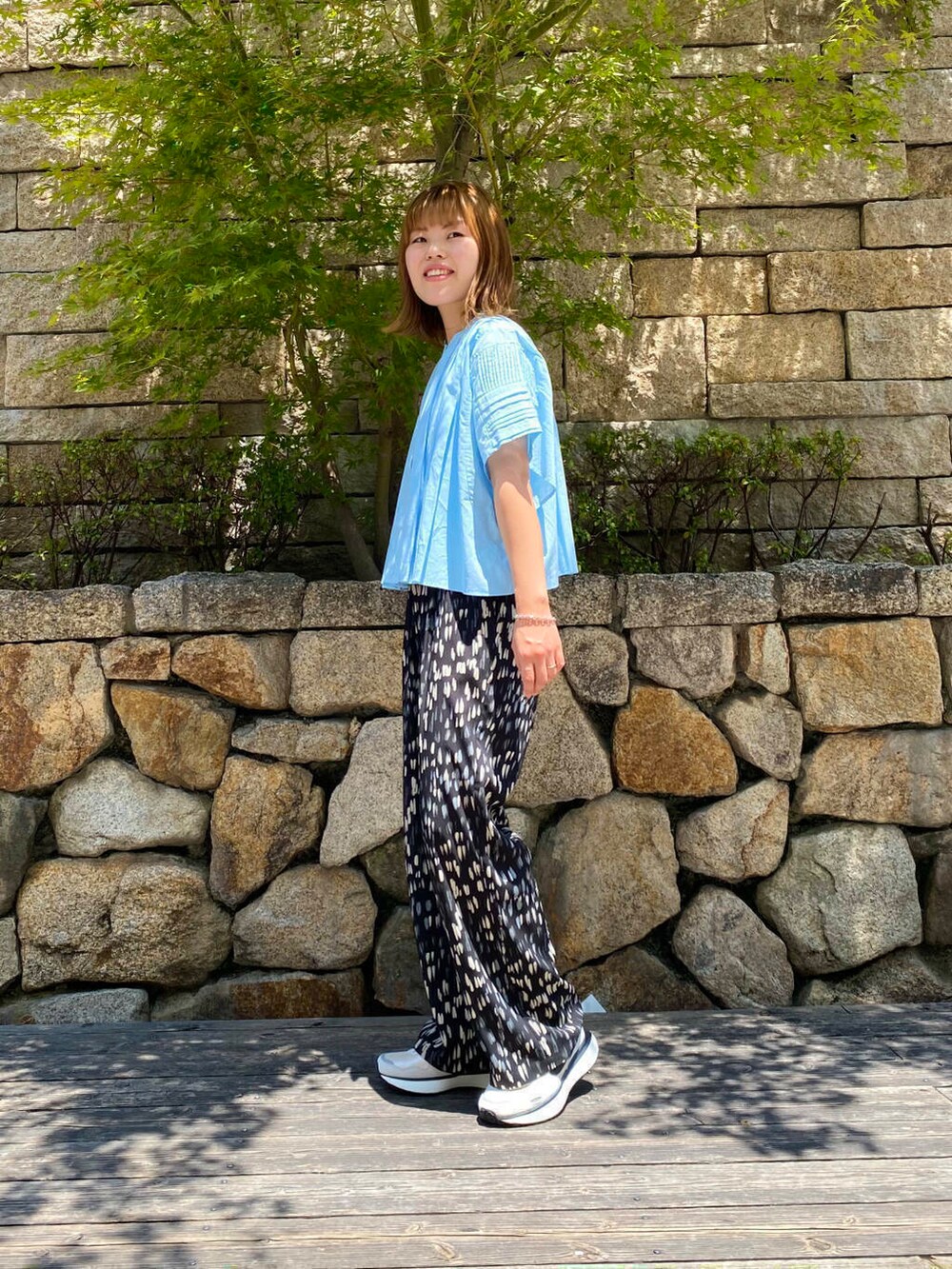 グレー系のショルダーバッグ、ホワイト系のスニーカー、ブルー系のシャツ/ブラウスを着用したレディースの夏コーディネートの3枚目の写真