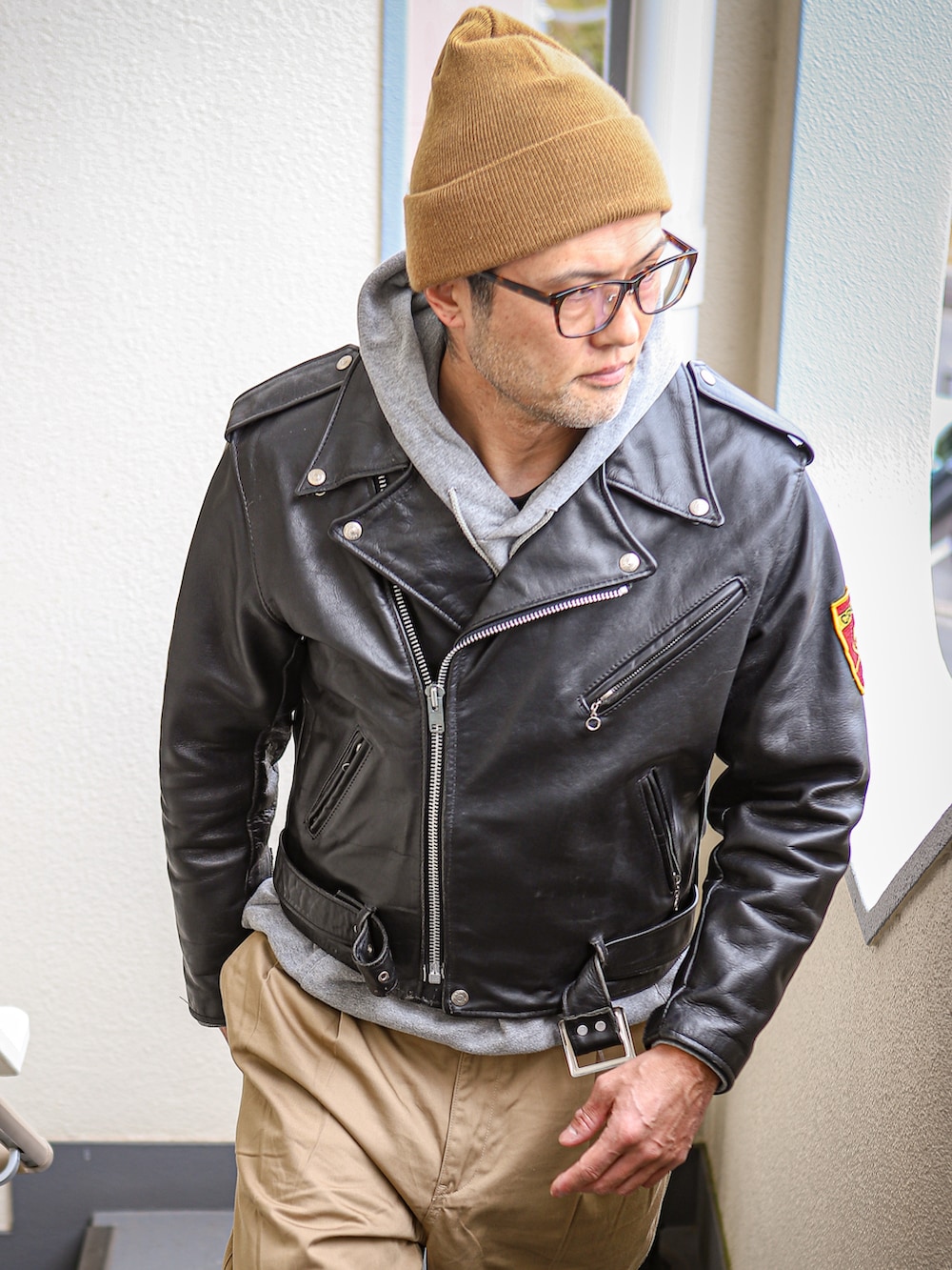 ブラック系のライダースジャケット、グレー系のパーカー、ベージュ系のチノパンツを着用したメンズの冬コーディネートの2枚目の写真