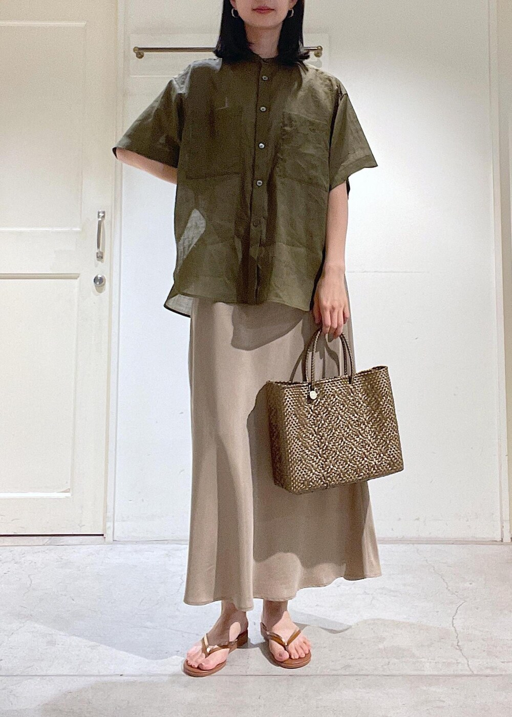 ブラウン系のサンダル、ベージュ系のスカート、ゴールド系のかごバッグを着用したレディースの春コーディネートの4枚目の写真