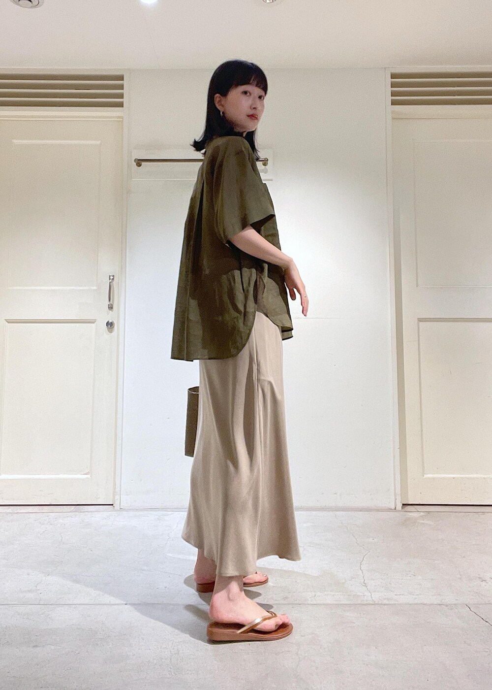 ブラウン系のサンダル、ベージュ系のスカート、ゴールド系のかごバッグを着用したレディースの春コーディネートの2枚目の写真