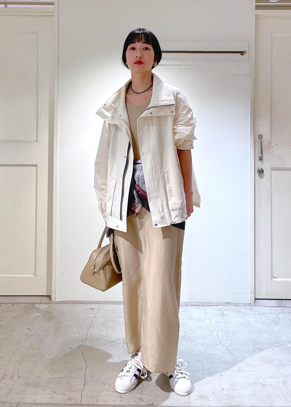 ベージュ系のワンピース、ホワイト系のブルゾン、ホワイト系のスニーカーを着用したレディースの冬コーディネートの2枚目の写真