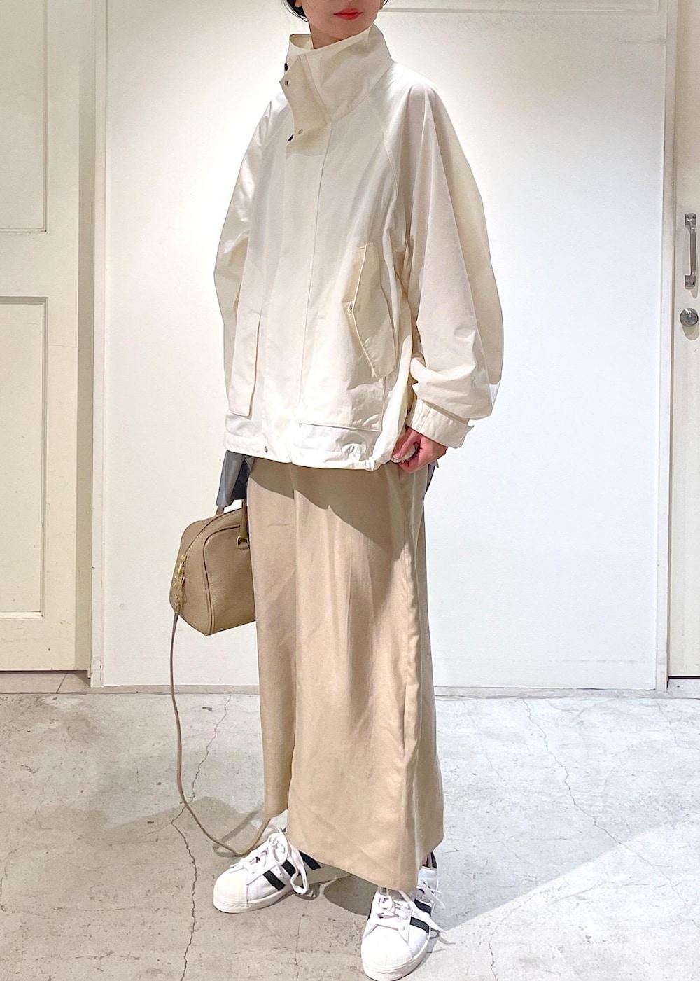 ベージュ系のワンピース、ホワイト系のブルゾン、ホワイト系のスニーカーを着用したレディースの冬コーディネートの3枚目の写真
