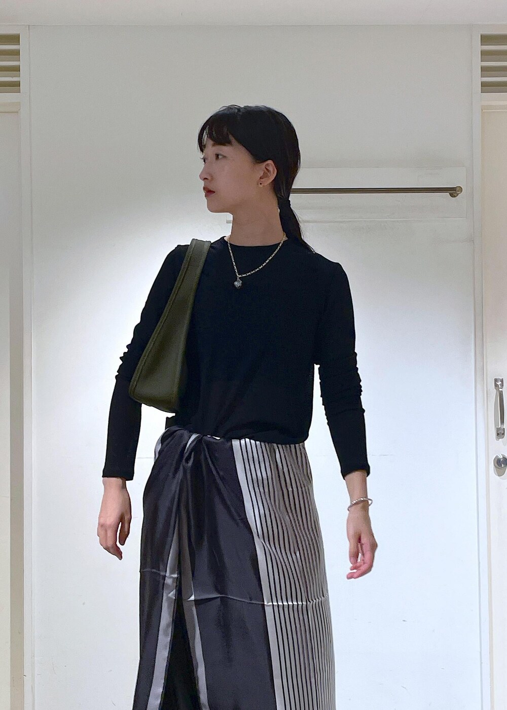 ブラック系のTシャツ/カットソー、グリーン系のハンドバッグ、ブラック系のブーツを着用したレディースの秋コーディネートの9枚目の写真