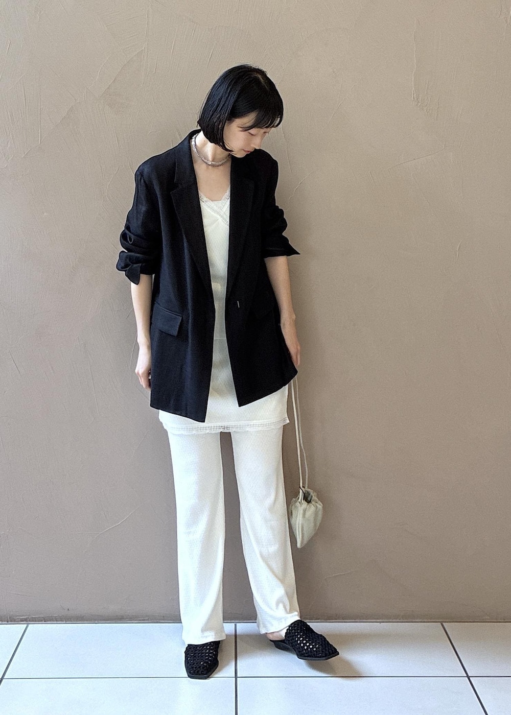 ブラック系のテーラードジャケット、ブラック系のサンダル、ホワイト系のキャミソールを着用したレディースの春コーディネートの2枚目の写真