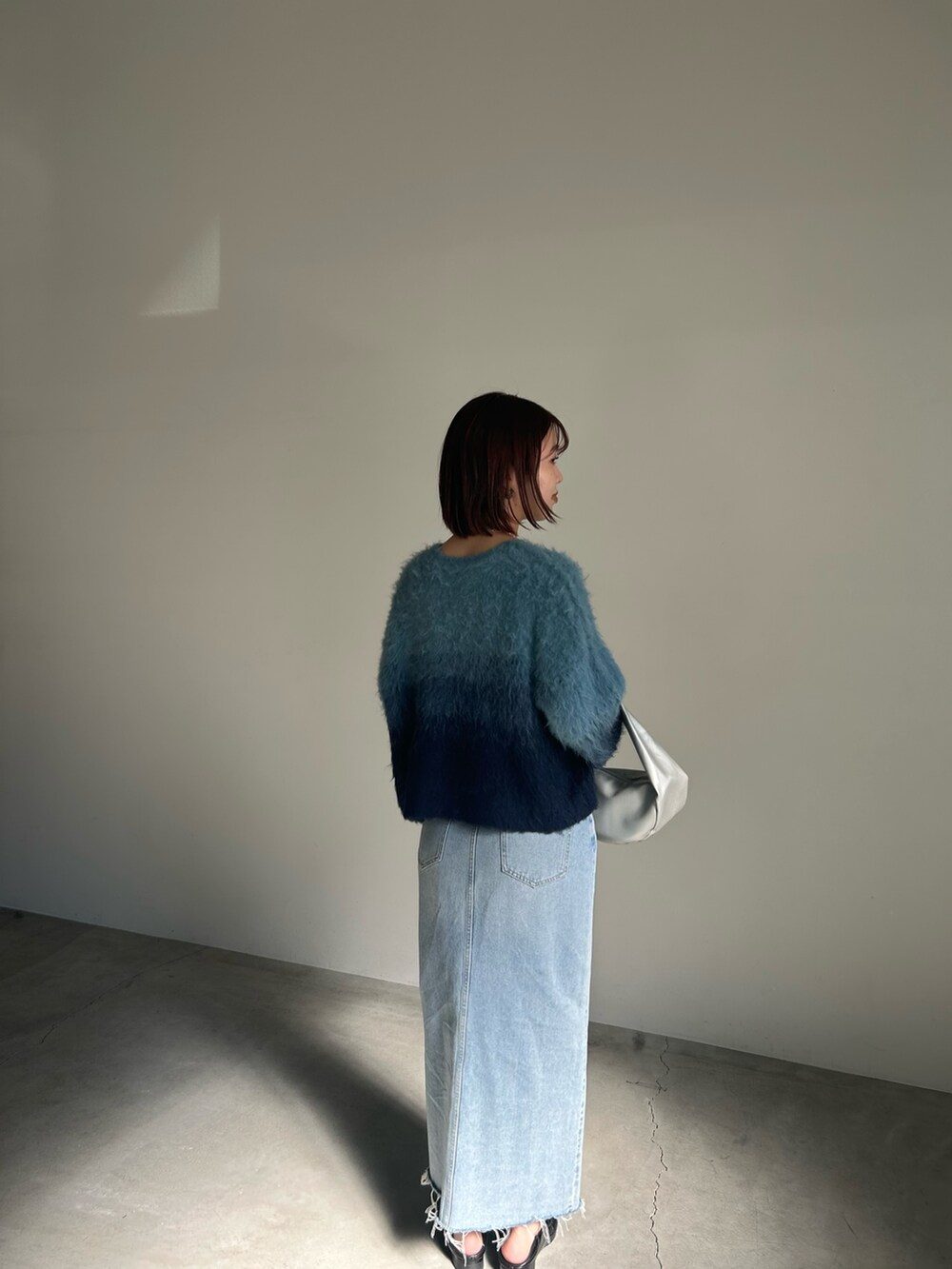 ブルー系のニット/セーター、ブルー系のデニムスカート、シルバー系のショルダーバッグを着用したレディースの夏コーディネートの2枚目の写真