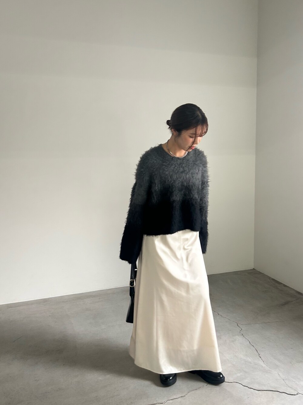 ブラック系のニット/セーター、ブラック系のハンドバッグ、ホワイト系のスカートを着用したレディースの秋コーディネートの3枚目の写真