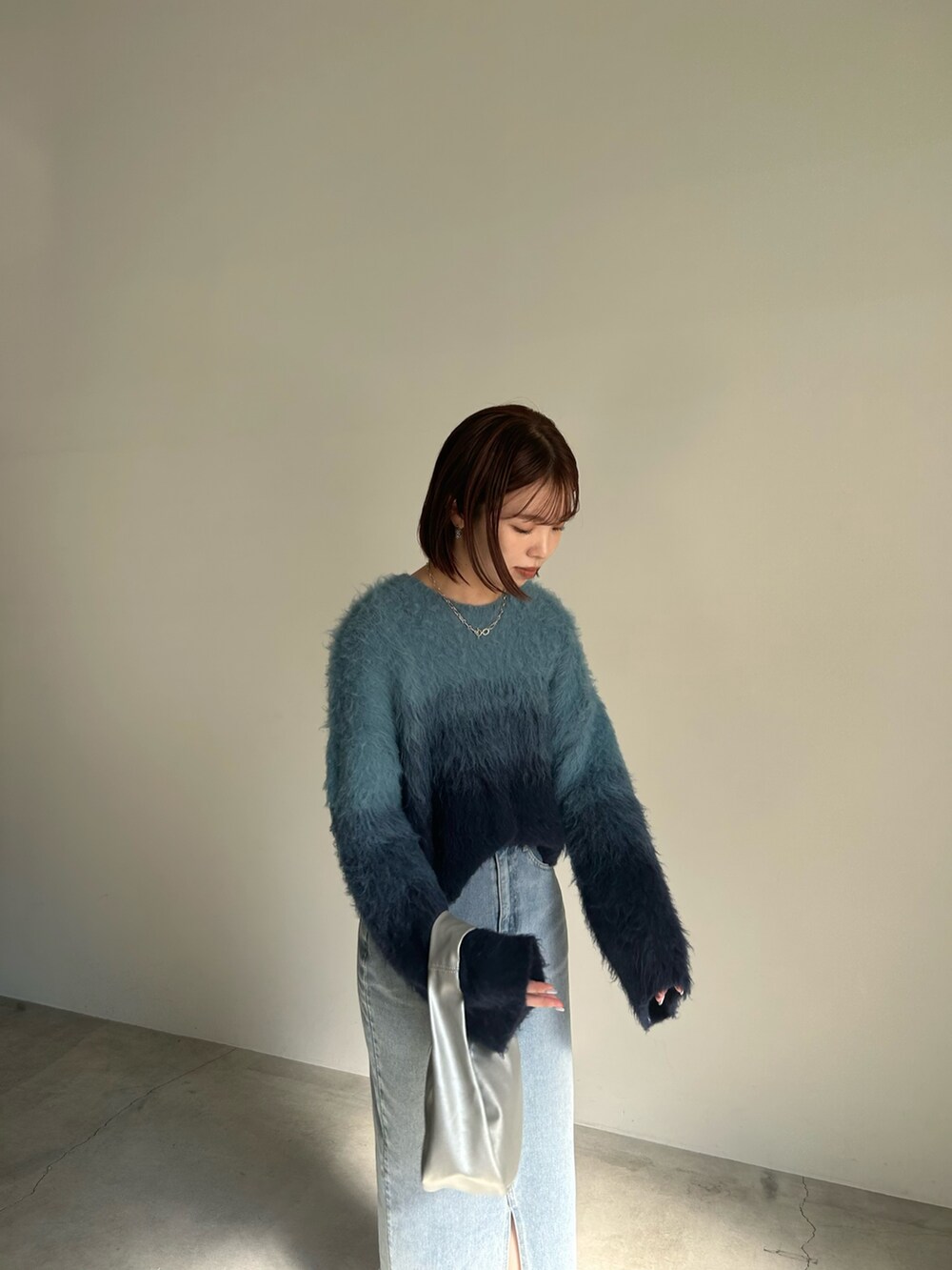 ブルー系のニット/セーター、ブルー系のデニムスカート、シルバー系のショルダーバッグを着用したレディースの夏コーディネートの3枚目の写真