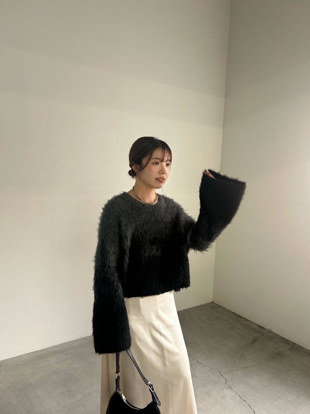 ブラック系のニット/セーター、ブラック系のハンドバッグ、ホワイト系のスカートを着用したレディースの秋コーディネートの2枚目の写真