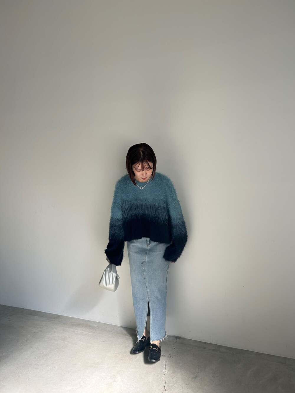 ブルー系のニット/セーター、ブルー系のデニムスカート、シルバー系のショルダーバッグを着用したレディースの夏コーディネートの4枚目の写真