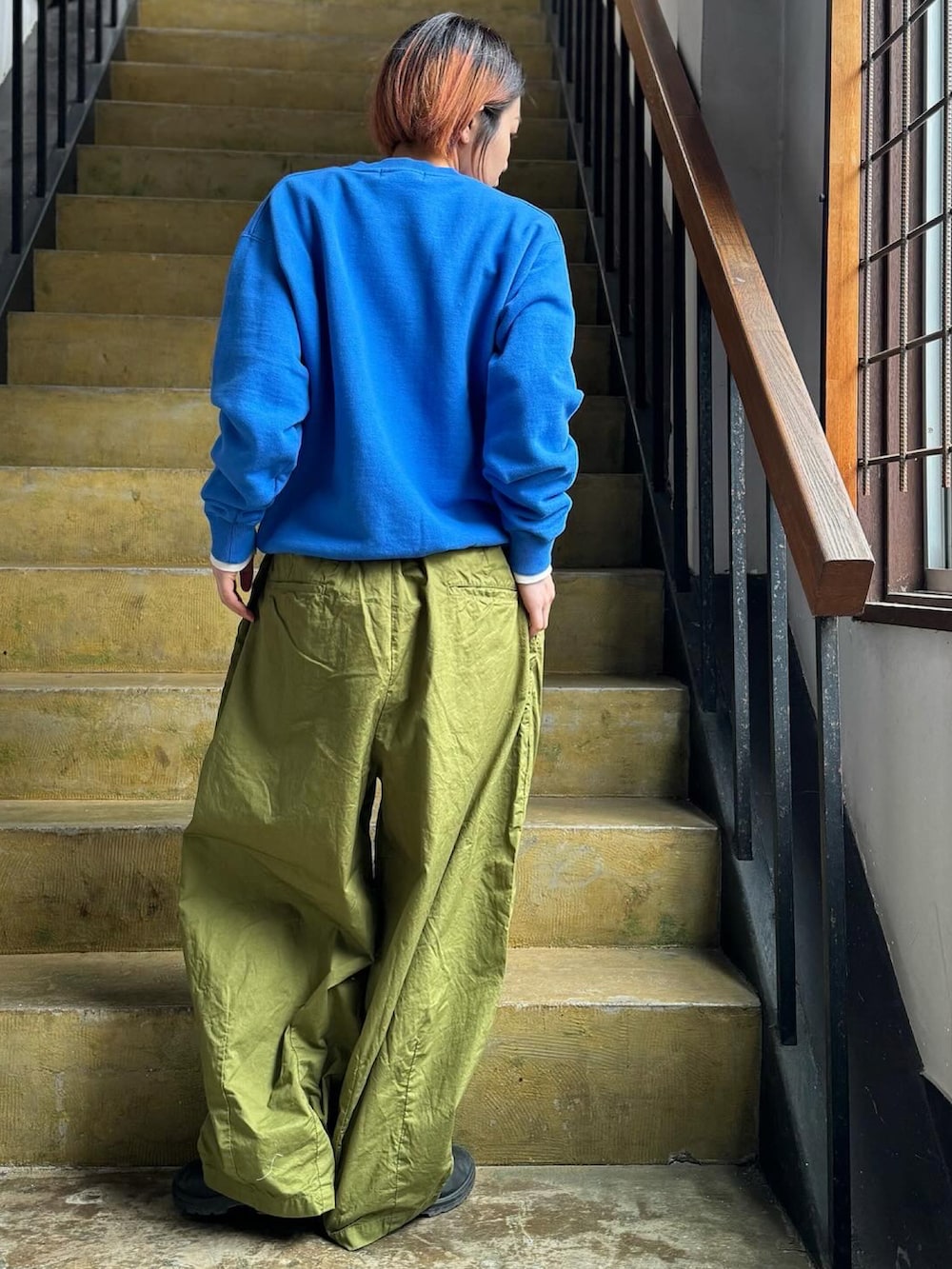 ブルー系のスウェット、グリーン系のパンツ、ブラック系のレインシューズを着用したレディースの冬コーディネートの2枚目の写真