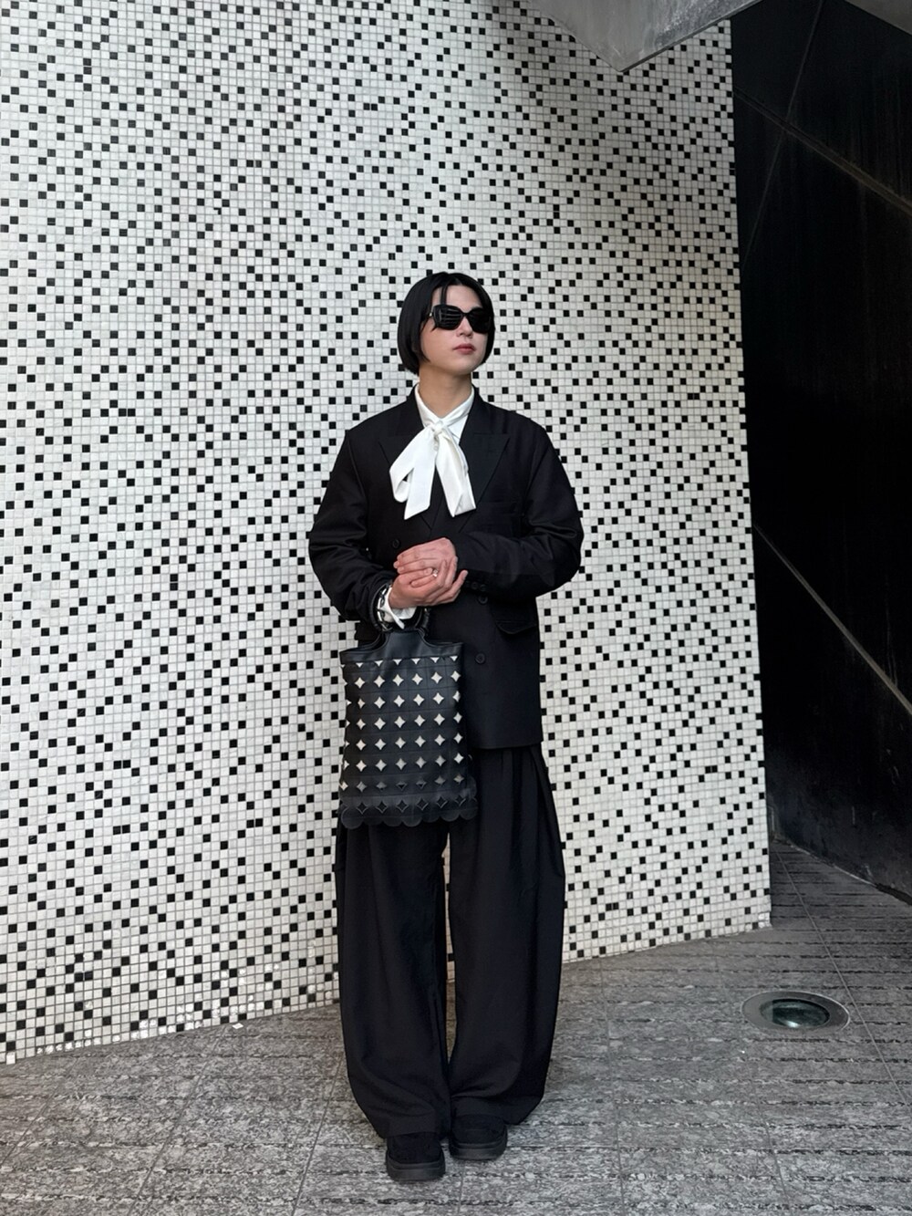 ブラック系のテーラードジャケット、ブラック系のトートバッグ、ブラック系のスラックスを着用したメンズの春コーディネートの2枚目の写真