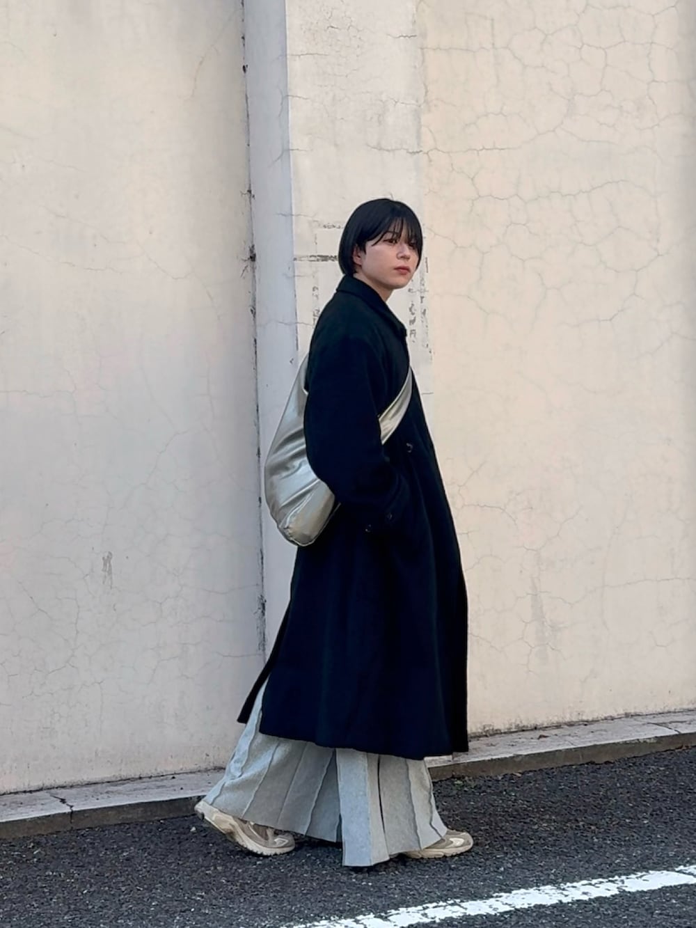 シルバー系のトートバッグ、ブラック系のチェスターコート、グレー系のスウェットパンツを着用したメンズの春コーディネートの2枚目の写真