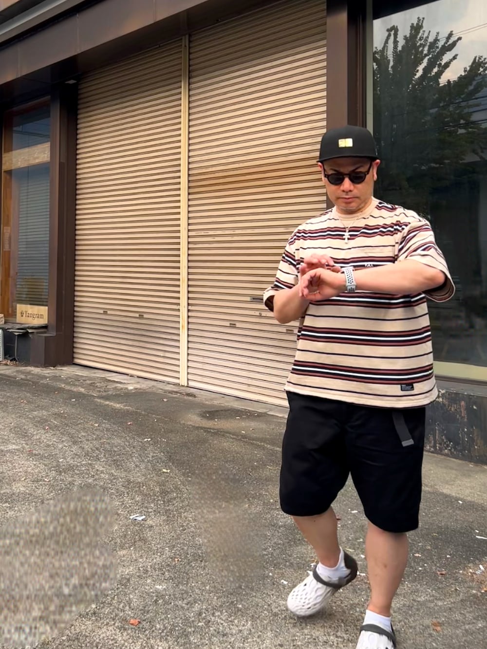 ブラック系のチノパンツ、ブラウン系のTシャツ/カットソー、ホワイト系のサンダルを着用したメンズの夏コーディネートの2枚目の写真