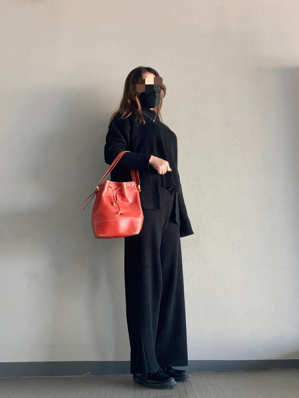 ブラック系のニット/セーター、オレンジ系のバッグ、ブラック系のブーツを着用したレディースの秋コーディネートの2枚目の写真