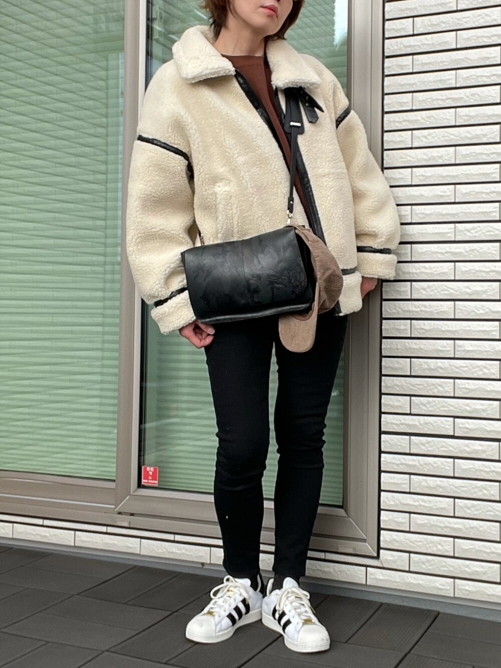 ブラック系のムートンコート、ブラウン系のスウェット、ブラック系のデニムパンツを着用したレディースの冬コーディネートの3枚目の写真